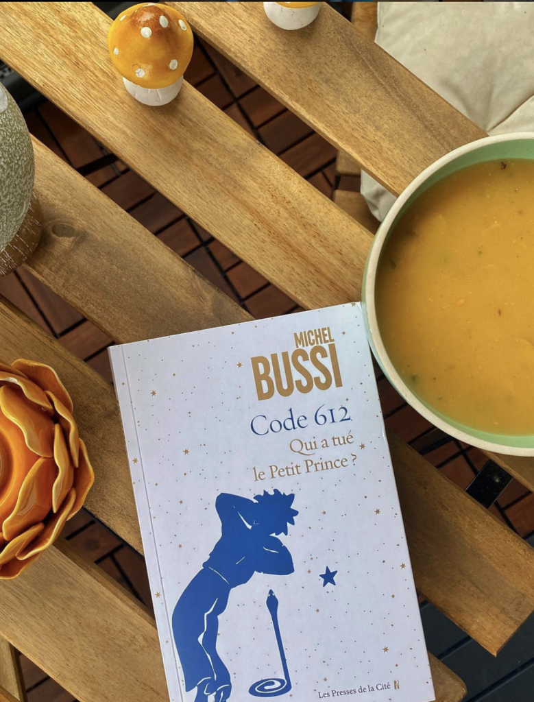 Livre Code 612 : Qui a tué le Petit Prince ? de Michel Bussi posé sur une table en bois, accompagné d’une soupe de courges et de petites décorations automnales, évoquant une lecture cocooning de saison.