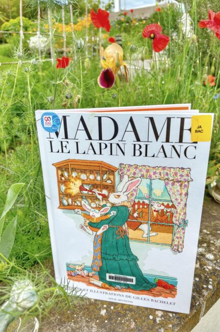 Madame le lapin blanc Gilles Bachelet devant un jardin en fleurs