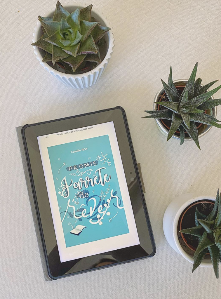 Tablette affichant la couverture du roman Promis j’arrête de rêver de Camille Roy, entourée de petites plantes grasses sur une table claire.