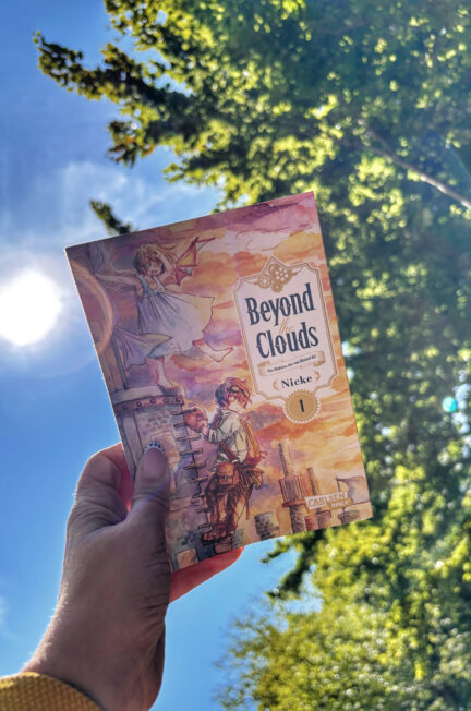Le tome 1 de la saga Beyond the clouds de Nicke, intitulé La fillette tombée du ciel, tenu devant le ciel bleu avec le soleil, une traînée de nuage et un arbre en arrière-plan