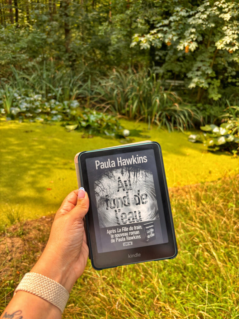 Au fond de l'eau de Paula Hawkins sur une liseuse Kindle devant un étang recouvert de mousse dans une forêt