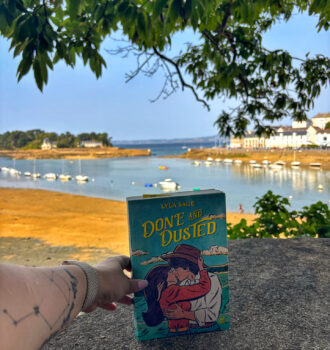Main tenant Done and Dusted de Lyla Sage devant une vue sur l'île Tristan et la baie de Douarnenez