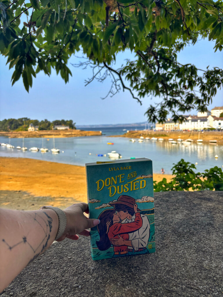 Main tenant Done and Dusted de Lyla Sage devant une vue sur l'île Tristan et la baie de Douarnenez