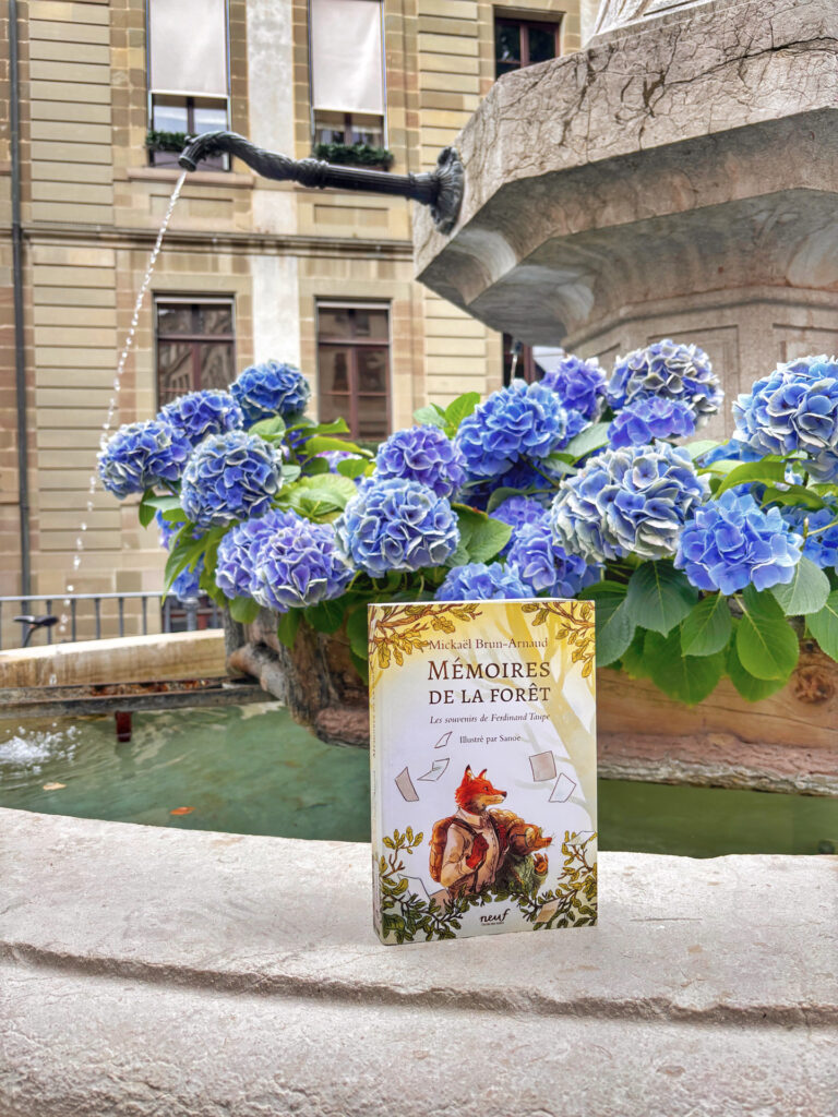 Photo du roman jeunesse "Mémoires de la forêt – Les souvenirs de Ferdinand Taupe" de Mickaël Brun-Arnaud, prise à Genève devant une fontaine décorée d’hortensias bleus.