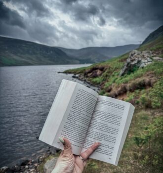 Page ouverte de La sœur de l’ombre de Lucinda Riley tenue face au Loch Lee, avec les montagnes écossaises sous un ciel orageux.