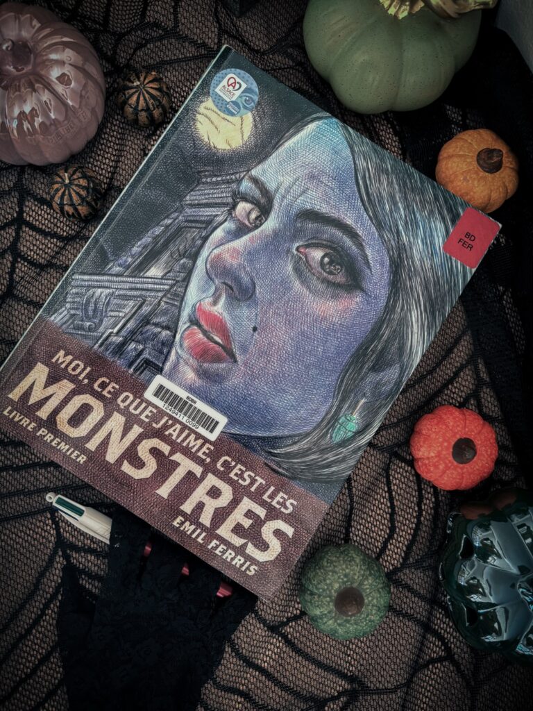 Couverture du roman graphique Moi, ce que j’aime, c’est les monstres – livre premier – d’Emil Ferris, photographié sur une nappe toile d’araignée avec des citrouilles décoratives d’Halloween.