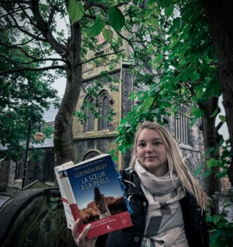Devant la Parish Church de Leith, livre La sœur à la perle de Lucinda Riley en main, entre végétation dense et architecture ancienne – Sur les traces des Sept Sœurs.
