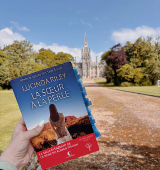 Photo du roman La sœur à la perle de Lucinda Riley tenu à bout de bras devant la majestueuse façade du Fettes College, baignée par le soleil écossais et entourée d’un vaste parc.