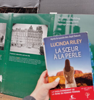 Photo du roman La sœur à la perle tenu devant les palissades du magasin Jenners sur Princes Street, recouvertes de photos d’archives en noir et blanc annonçant la restauration du bâtiment historique.