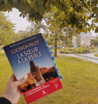 Photo du roman La sœur à la perle dans un parc verdoyant d’Édimbourg, sous les arbres trempés par la pluie écossaise, avec les immeubles historiques de la ville en arrière-plan.