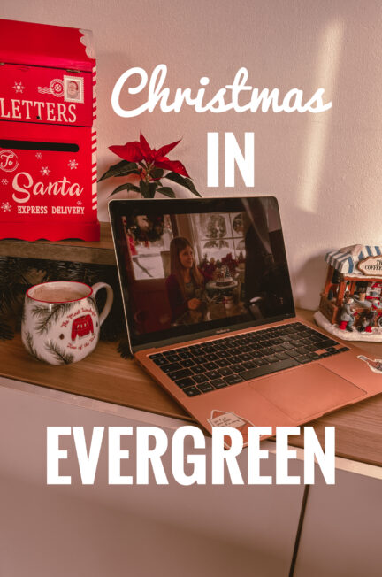 Un ordinateur portable posé sur un meuble diffuse une scène du premier Christmas in Evergreen. À côté, une tasse décorée, une guirlande de sapin et une petite maison de village enneigé sont disposées. Sur la gauche, une grande boîte rouge en forme de boîte aux lettres indique Letters to Santa.