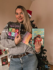 Sorbet-Kiwi tient trois ouvrages inspirés de Taylor Swift. On voit notamment Into the Taylor-Verse et deux romans aux couvertures colorées. Le sapin décoré apparaît à l’arrière-plan. - Cadeaux pour Swifties