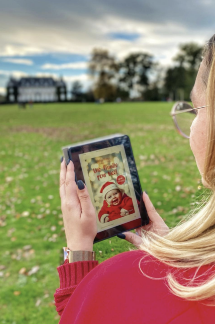 Sorbet-Kiwi de dos lit le roman numérique « Une famille pour Noël » sur une liseuse, dans un parc verdoyant avec un grand château en arrière-plan, par une journée d’automne.