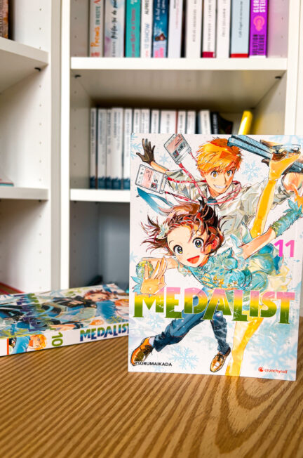 Couverture du manga Medalist tome 11 de Tsurumaikada, montrant Inori et Tsukasa en tenue de patinage artistique, posée devant une bibliothèque.