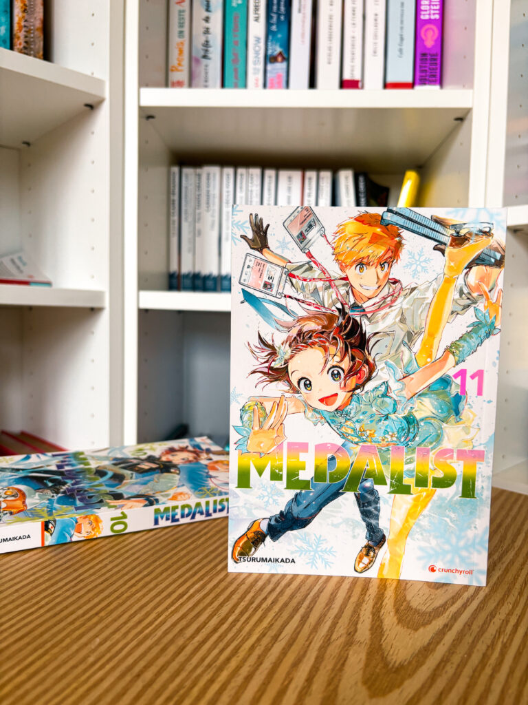 Couverture du manga Medalist tome 11 de Tsurumaikada, montrant Inori et Tsukasa en tenue de patinage artistique, posée devant une bibliothèque.