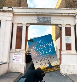 Exemplaire du roman The Shadow Sister de Lucinda Riley tenu devant l’arche de l’ancien hôpital des mères de l’Armée du Salut à Londres, lieu lié aux origines de Star.