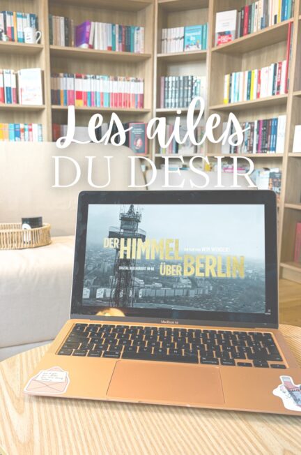 Ordinateur portable diffusant le film Les ailes du désir posé sur une table en bois, devant une grande bibliothèque remplie de livres, dans un salon lumineux.