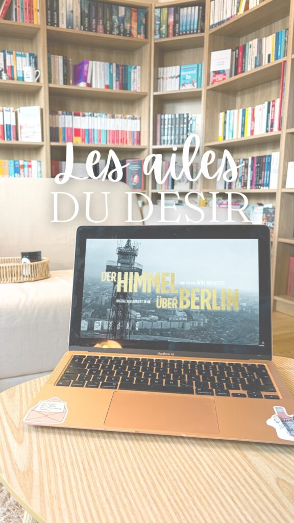 Ordinateur portable diffusant le film Les ailes du désir posé sur une table en bois, devant une grande bibliothèque remplie de livres, dans un salon lumineux.