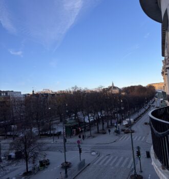 Vue plongeante sur la Grand Place d’Oslo bordée d’arbres sans feuilles et de bâtiments modernes, sous un ciel dégagé. Une ambiance hivernale typique de février, sur les traces d’Ally.