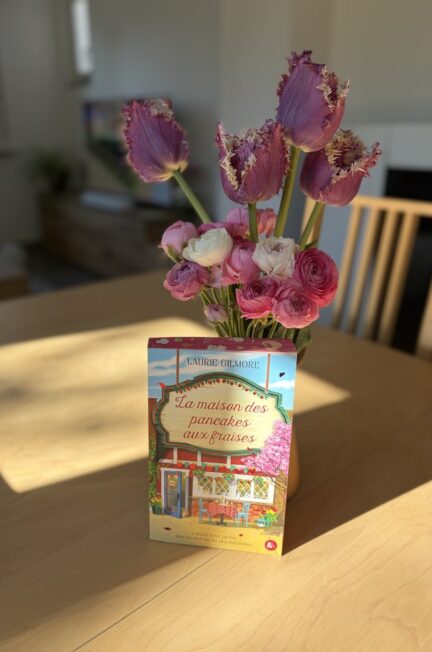 livre La maison des pancakes aux fraises posé sur une table en bois avec bouquet de tulipes roses et fleurs printanières en arrière plan