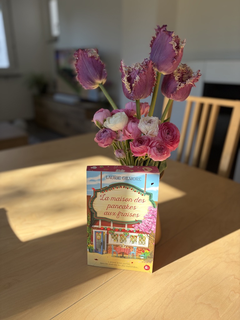 livre La maison des pancakes aux fraises posé sur une table en bois avec bouquet de tulipes roses et fleurs printanières en arrière plan
