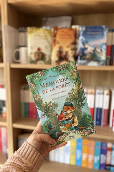 Le dernier tome de la saga des Mémoires de la forêt intitulé La saison des adieux tenu en main devant une bibliothèque remplie de livres