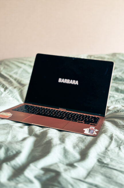 Ordinateur portable rose affichant le titre du film Barbara sur un lit aux draps verts, dans une ambiance douce et minimaliste.