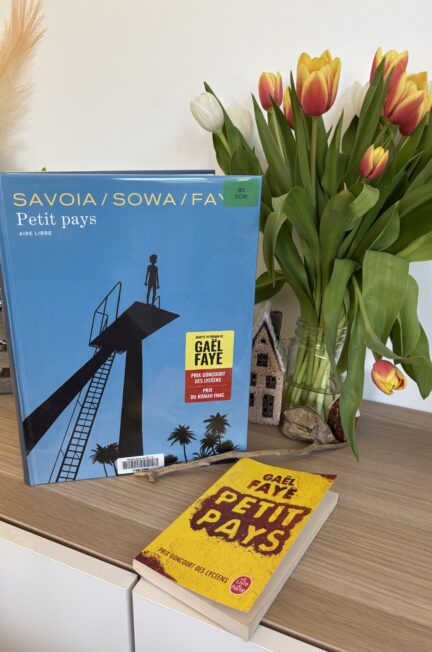 La BD Petit Pays de Gael Faye, Marzen Sowa et Sylvain Savoia posée à côté du roman de Gael Faye sur un meuble en bois, avec un bouquet de tulipes jaunes, rouges et blanches en arrière-plan.