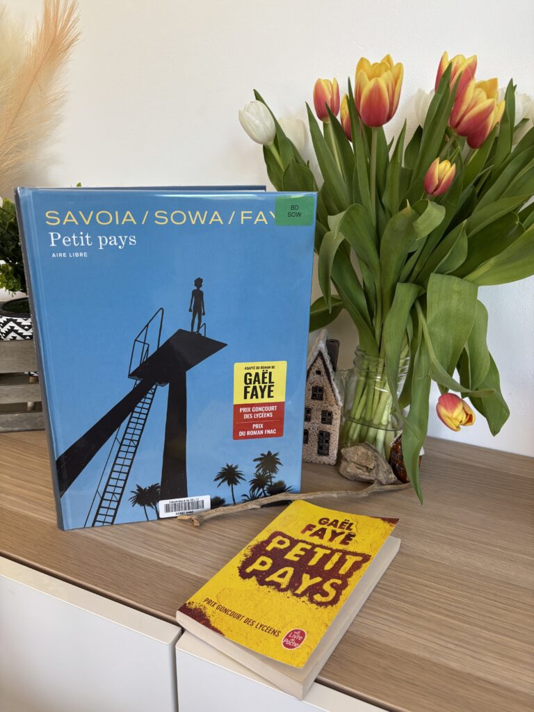 La BD Petit Pays de Gael Faye, Marzen Sowa et Sylvain Savoia posée à côté du roman de Gael Faye sur un meuble en bois, avec un bouquet de tulipes jaunes, rouges et blanches en arrière-plan.