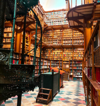 Bibliothèque vue centrale : Intérieur de la bibliothèque jésuite de Maria Laach avec ses étagères monumentales, ses escaliers métalliques et son sol en carreaux colorés.