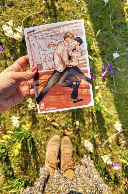 Le manga Afterschool Ballet de Hirune Cyan tenu à la main au-dessus d'un parterre de fleurs printanières, avec une robe fleurie et des chaussures visibles en arrière-plan.