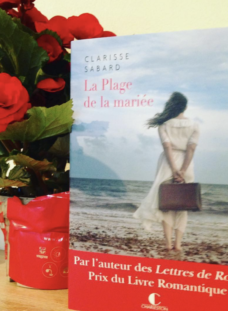 Le livre la plage de la mariée à côté d'un bouquet de fleurs rouges