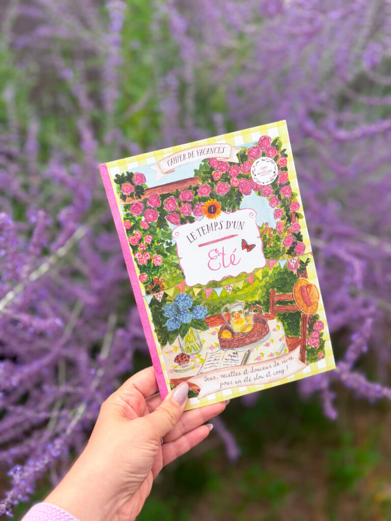 Le cahier de vacances Le temps d'un été de Caro From Woodland photographié devant un massif de fleurs violettes de mon jardin.