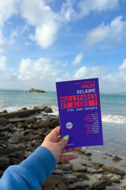 Le livre Nullipares et alors ? Être sans enfants, coordonné par Chloé Delaume, tenu à la main devant la plage de Tréboul à Douarnenez, en Bretagne.