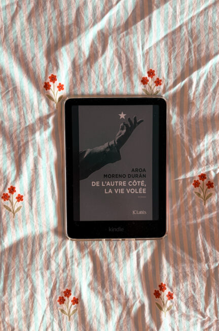 Le roman De l'autre côté la vie volée de Aroa Moreno Duran affiché sur une Kindle, posée sur une couette fleurie