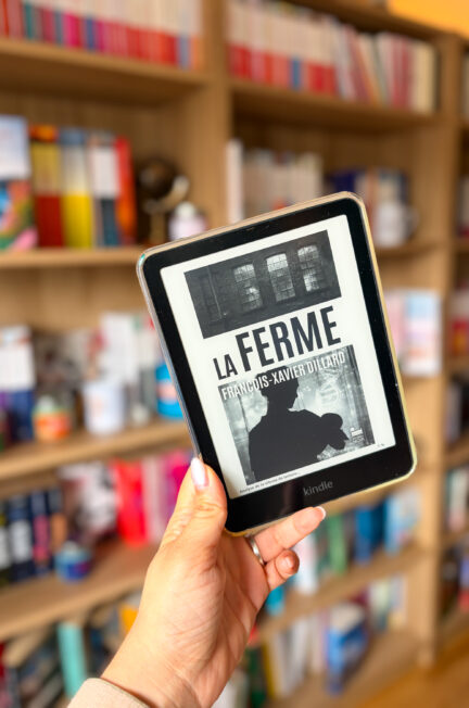 La ferme de François Xavier Dillard sur une liseuse tenue à la main devant une bibliothèque