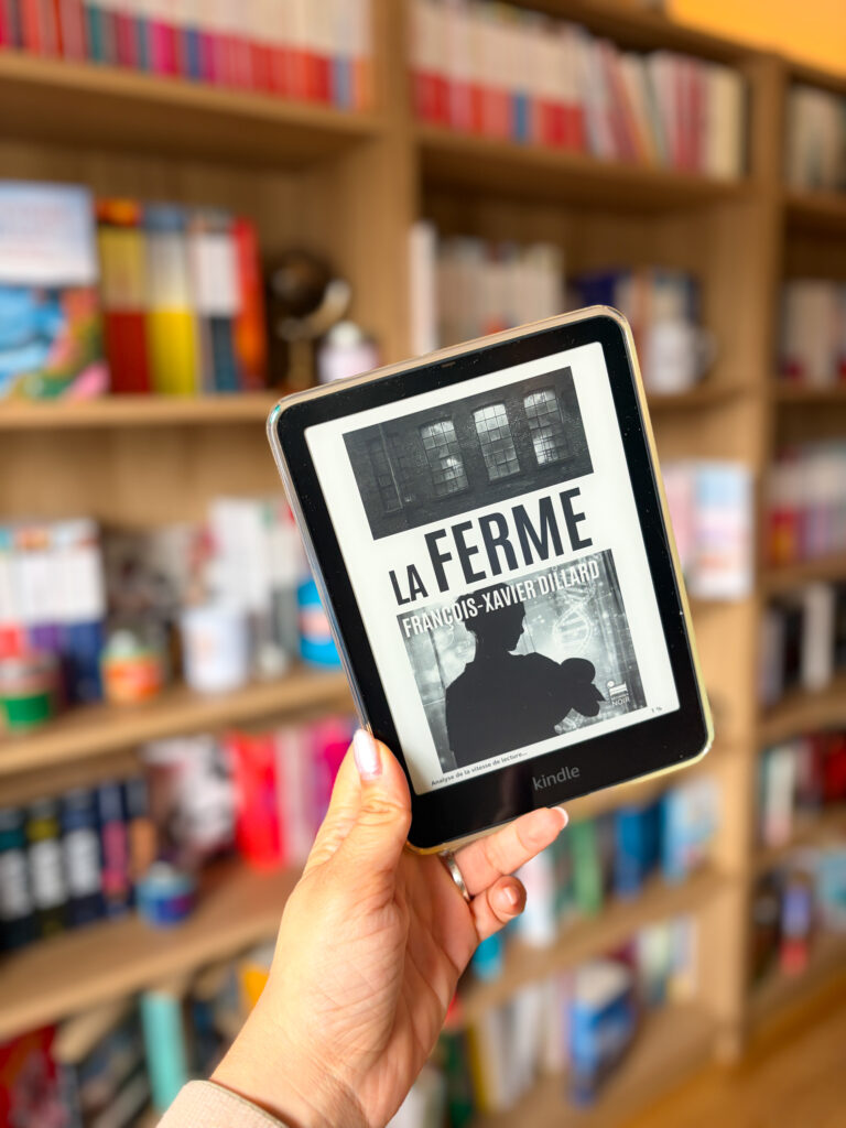 La ferme de François Xavier Dillard sur une liseuse tenue à la main devant une bibliothèque