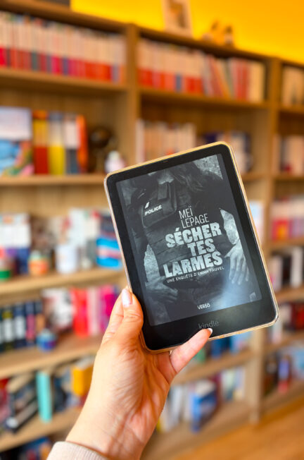 Le livre sécher tes larmes de Meï Lepage dont la couverture est affichée sur une Kindle devant une bibliothèque floutée en arrière-plan
