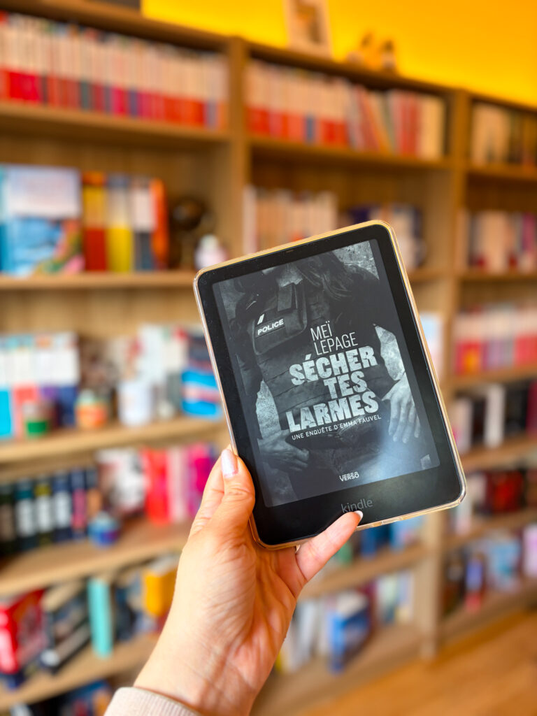 Le livre sécher tes larmes de Meï Lepage dont la couverture est affichée sur une Kindle devant une bibliothèque floutée en arrière-plan