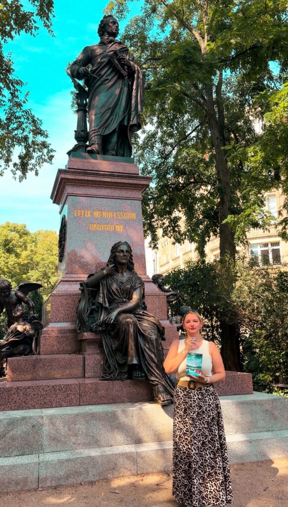 La nouvelle statue de Felix Mendelssohn Bartholdy à Leipzig, Sorbet-Kiwi se tenant devant avec le tome 2 des sept soeurs en main.