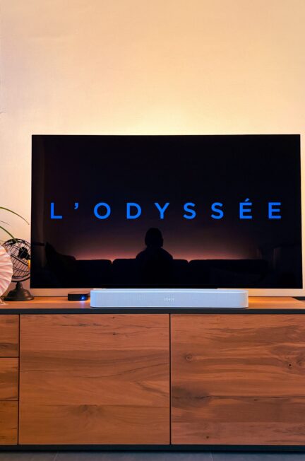 L'Odyssée de Christopher Nolan affiché sur une TV sur un meube en bois, rétroéclairé par une lumière douce, un globe à sa gauche