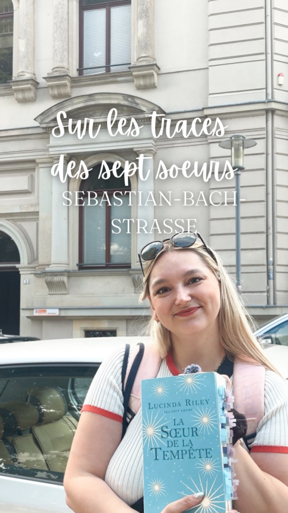 Sorbet-Kiwi tenant le tome 2 des sept soeurs dans ses mains devant une maison et le panneau indiquant la Sebastian Bach Strasse