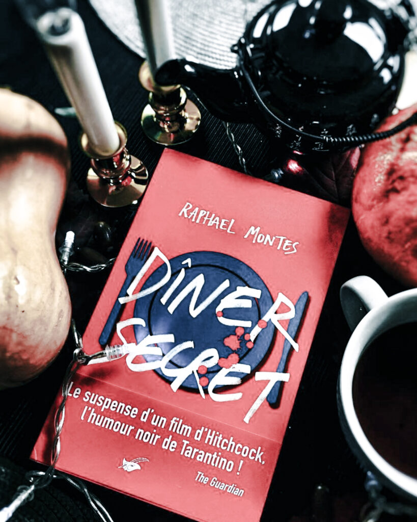 Dîner secret de Raphaël Montes posé sur une table sombre, entouré de bougies, d’un globe noir, de butternut, d’une tasse de café et de bougeoirs.
