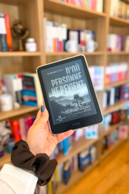 Kindle affichant la couverture de D’où personne ne revient de Clarence Pitz, tenue devant une bibliothèque remplie de livres.