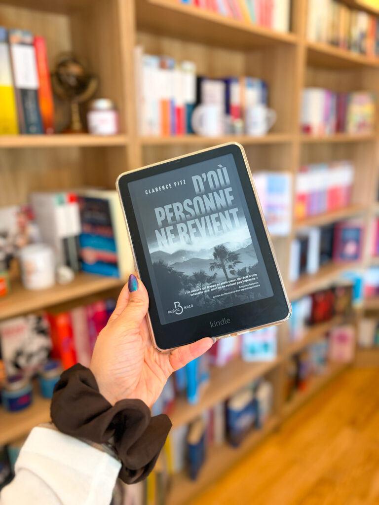 Kindle affichant la couverture de D’où personne ne revient de Clarence Pitz, tenue devant une bibliothèque remplie de livres.