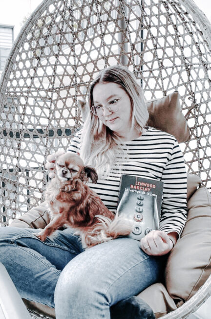 Femme assise dans un fauteuil suspendu avec un chien sur les genoux et Le vertige de la peur de Linwood Barclay à la main.