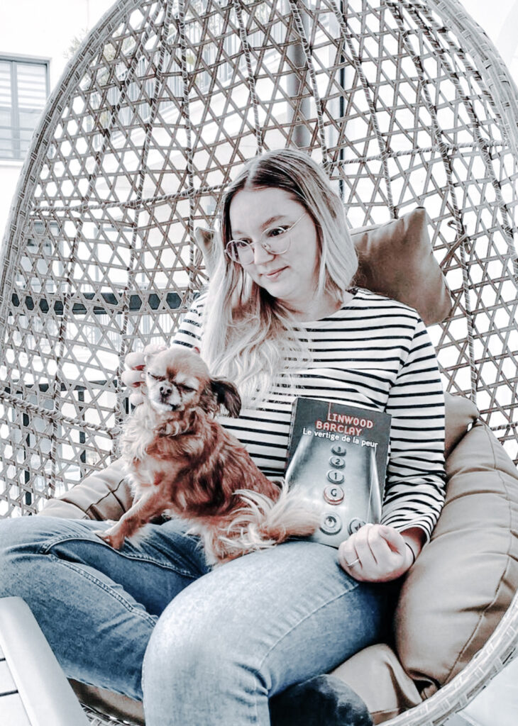 Femme assise dans un fauteuil suspendu avec un chien sur les genoux et Le vertige de la peur de Linwood Barclay à la main.