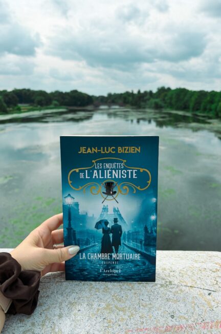 Livre La chambre mortuaire de Jean-Luc Bizien tenu à la main devant un plan d’eau bordé d’arbres à Leipzig.