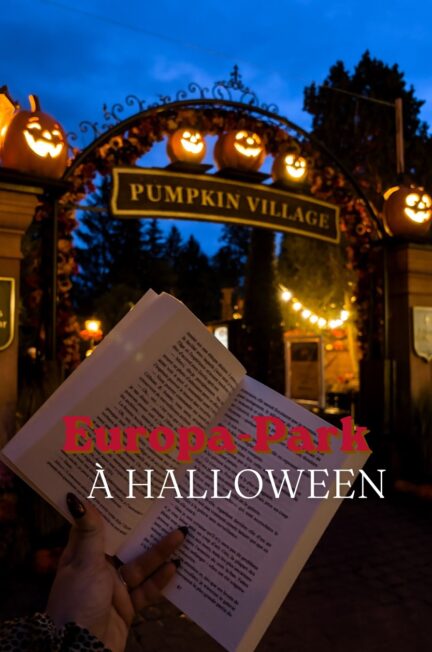 Photographie prise à Europa-Park pendant la saison d'Halloween 2026, à la tombée de la nuit. Au premier plan, une main tient un livre ouvert devant l'entrée du Pumpkin Village. L'arche décorative est ornée de citrouilles souriantes illuminées et de guirlandes automnales. À l'arrière-plan, les lumières du parc contrastent avec le ciel bleu profond. Le texte « Europa-Park à Halloween » est superposé à la photographie en rouge et blanc pour illustrer l'article de blog consacré à cette visite.