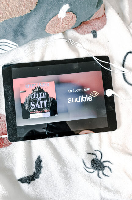 iPad qui affiche Celle qui sait de Riley Sager en écoute chez Audible posé sur un canapé avec un plaid action à citrouilles et araignées